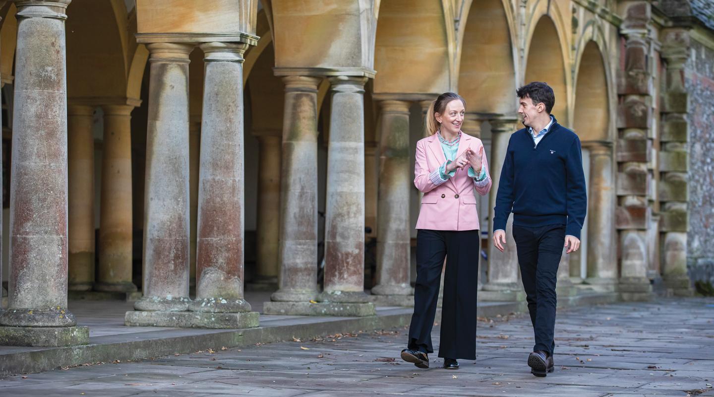 Emma Macey and Jack Andrews walking along chatting, in front of University of Oxford architecture
