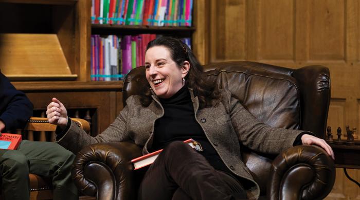 The Headmaster is sat in a leather chair, chatting and smiling with pupils.